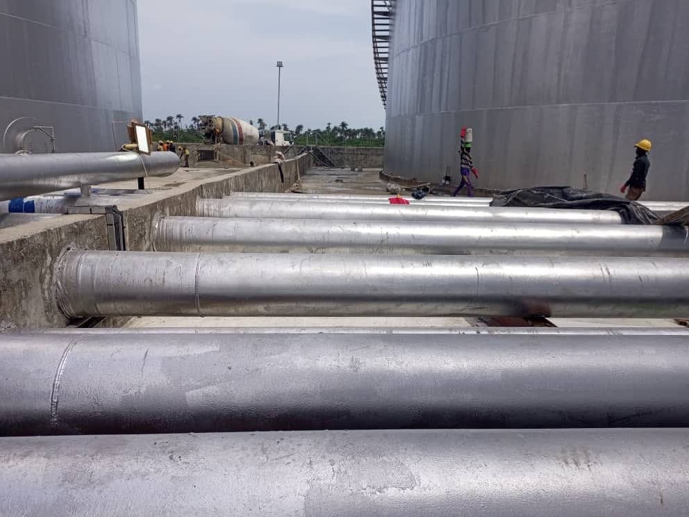 Large-diameter pipes crossing a concrete bund wall beside storage tanks