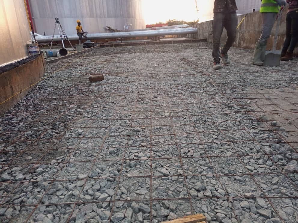 Reinforcement mesh laid over compacted stone while the crew prepares a concrete pour